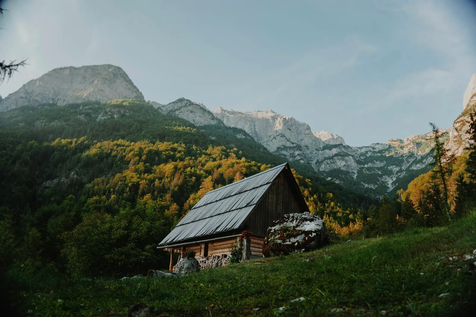 Cabaña de madera en la ladera de una montaña, con bosque y picos de piedra atrás
